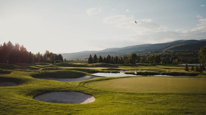 A golf course green with sand bunkers and mountains in the background