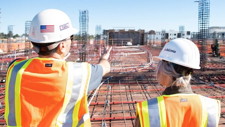Two construction workers in hard hats and safety vests reviewing a job site